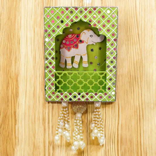 Decorative wall hanging with an elephant design in a green box on a wooden surface