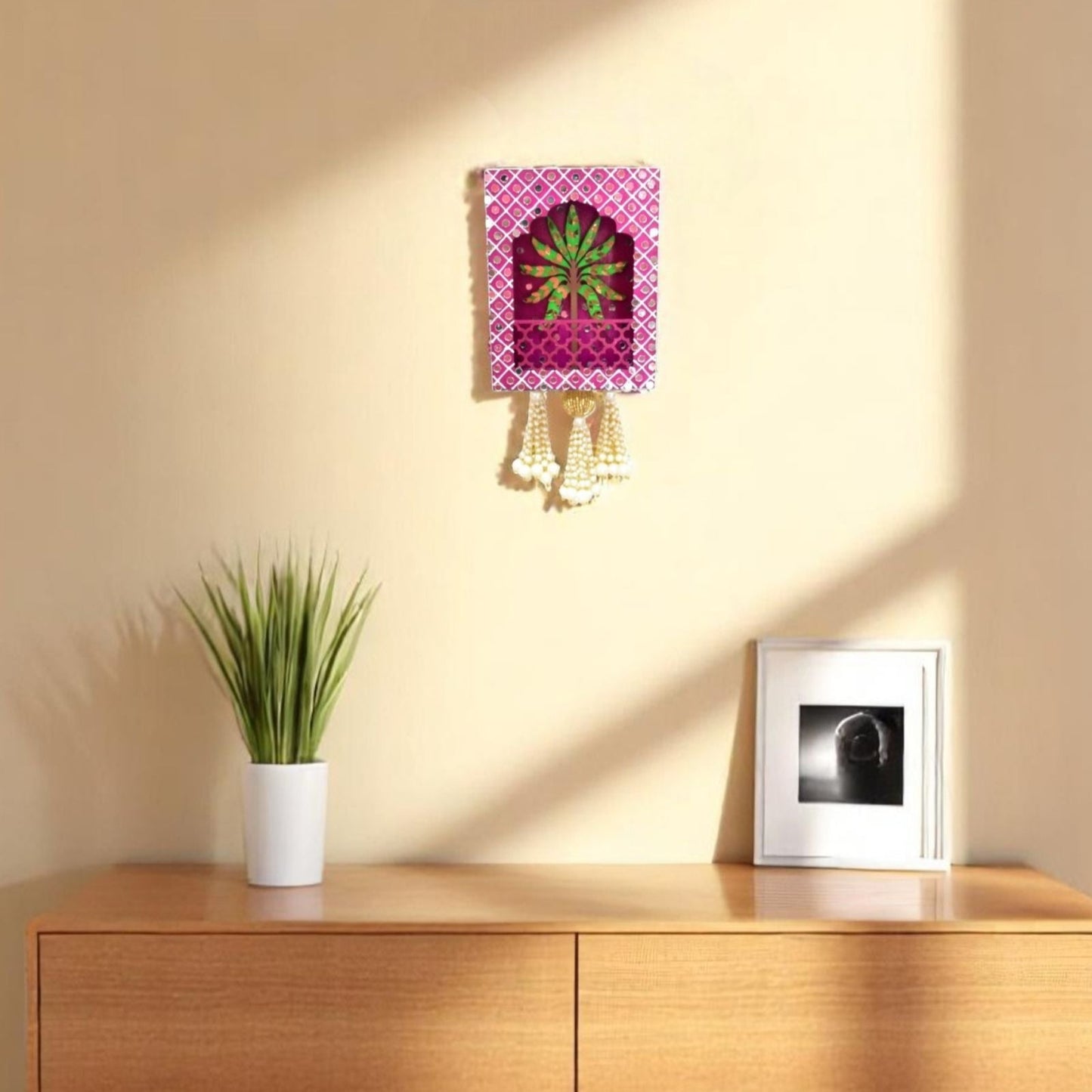 Decorative wall light fixture on a beige wall with a wooden cabinet and plant in the foreground.