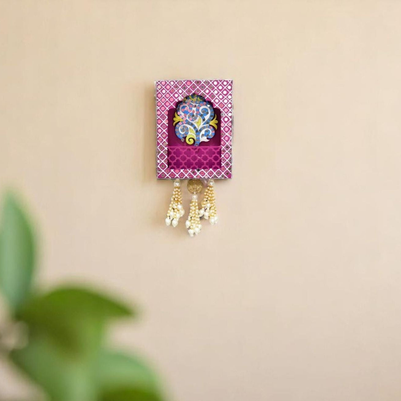 Decorative wall hanging with colorful design and hanging elements on a beige wall.