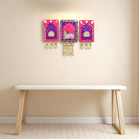 Three colorful wall hangings with decorative elements on a beige wall above a white table.