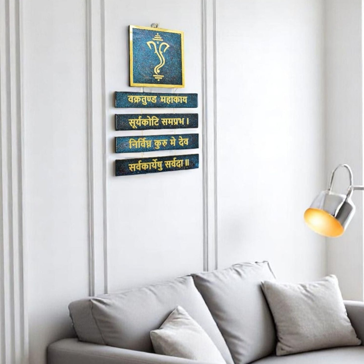 Decorative wall art with Ganesh and mantra on a white wall above a sofa.
