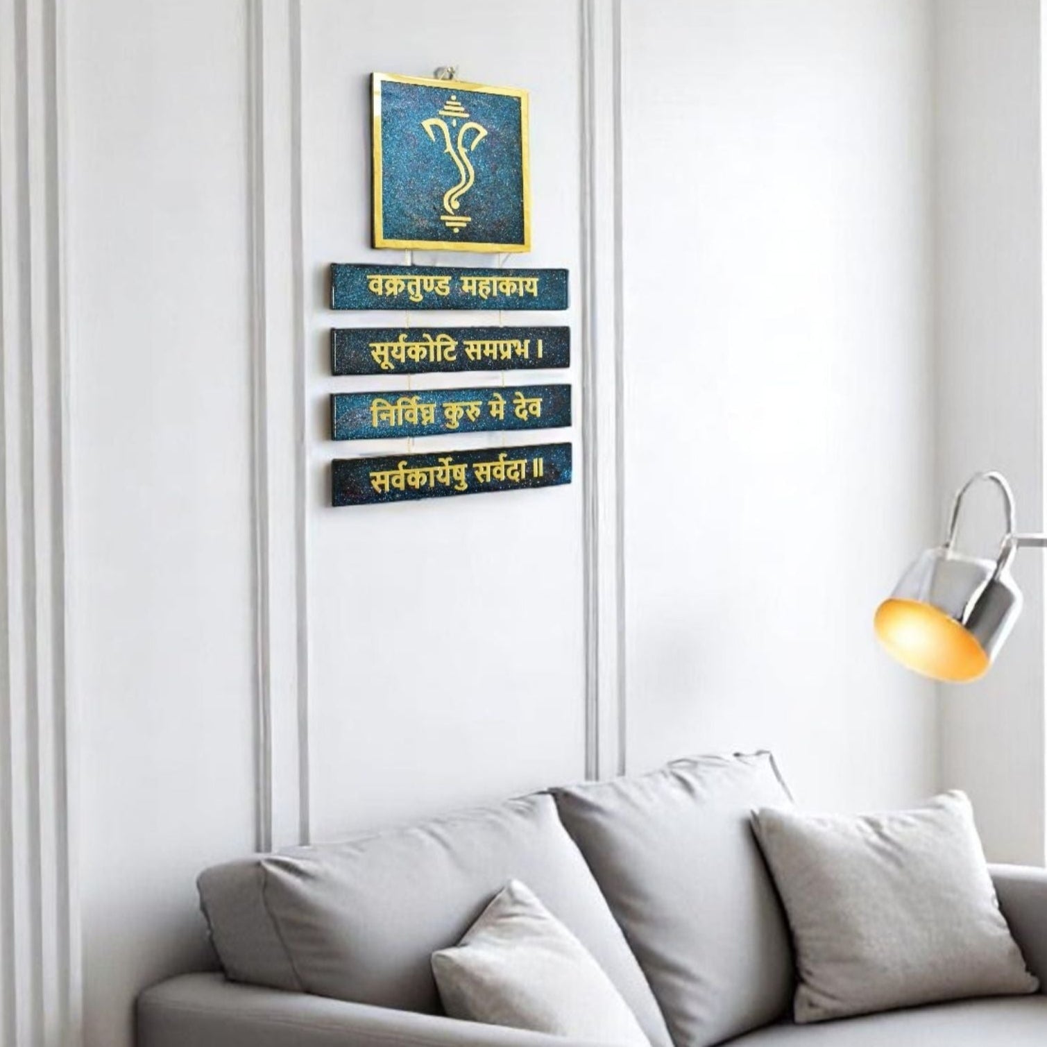 Decorative wall art with Ganesh and mantra on a white wall above a sofa.