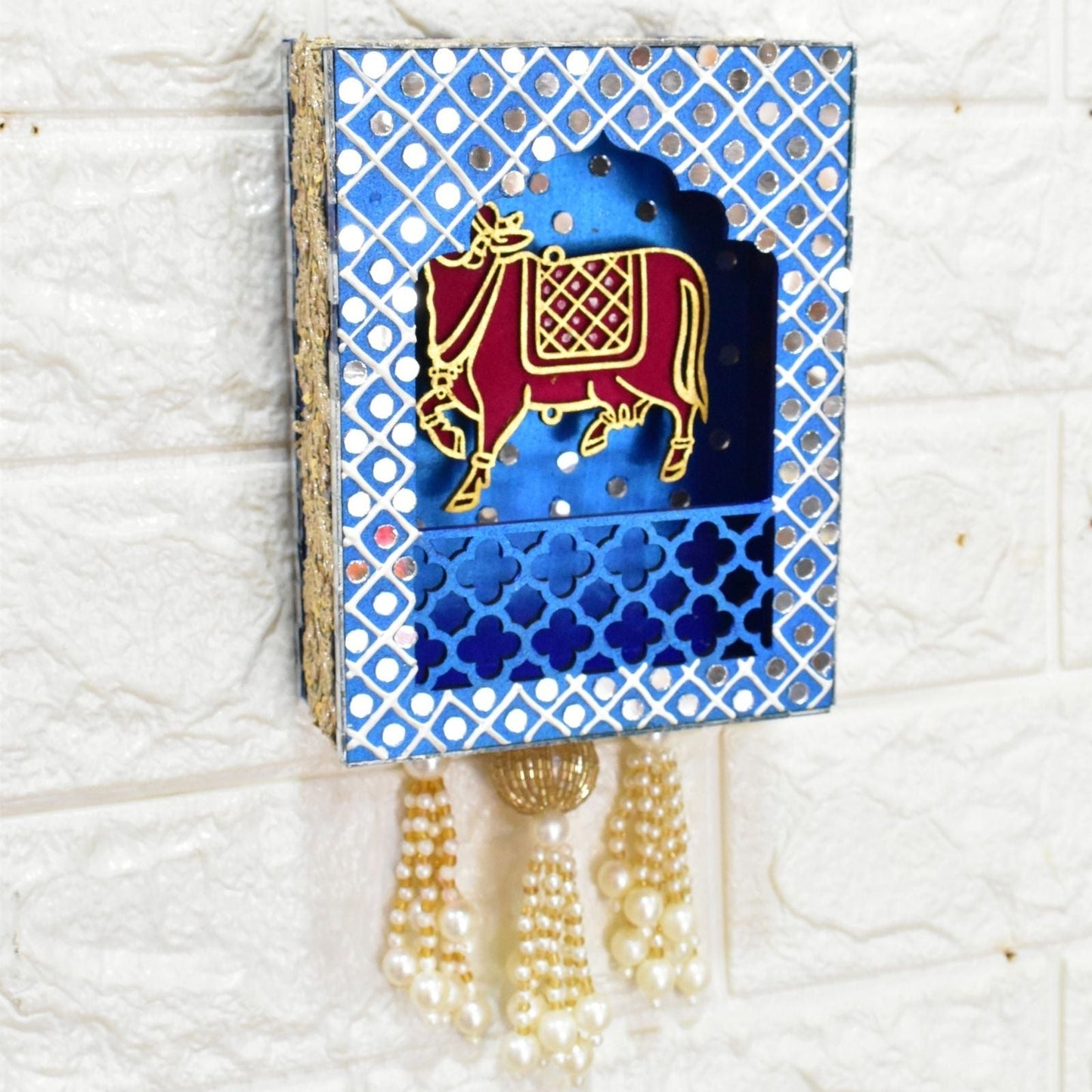 Decorative wall hanging with a blue patterned background and a gold cow illustration, on a white textured surface.