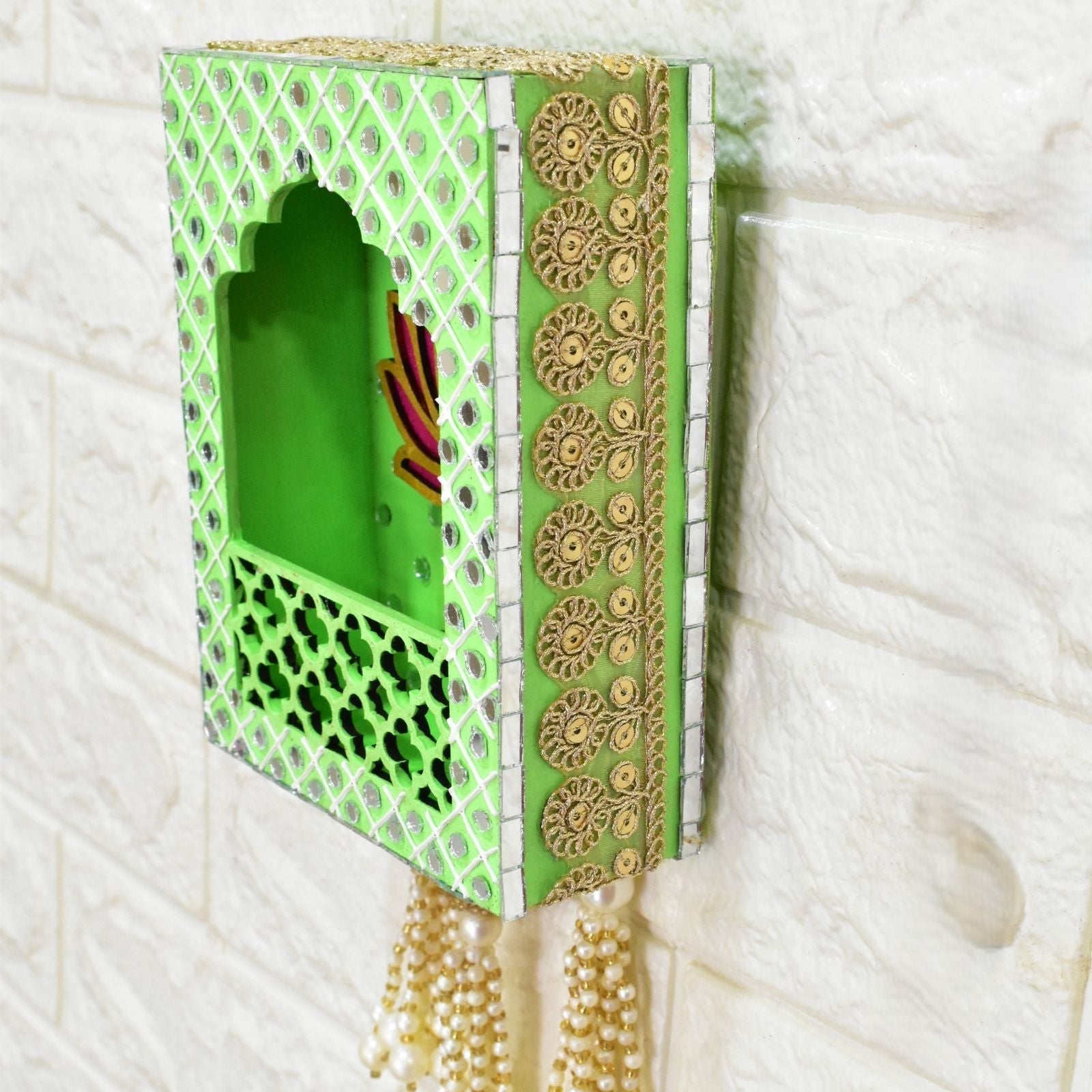 Decorative wall shelf with green and gold patterns and hanging pearls on a textured white background