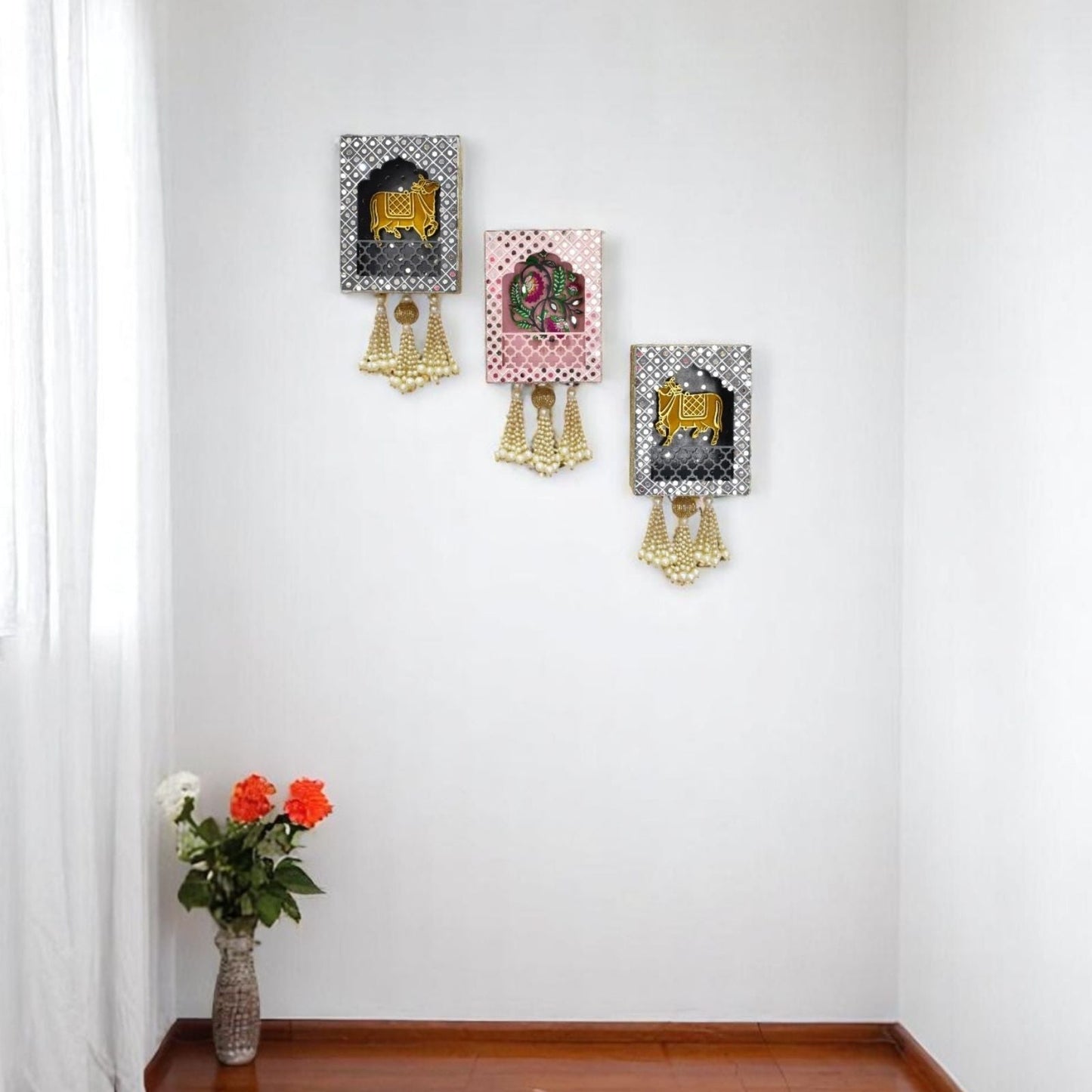 Decorative wall art pieces with gold accents on a white wall, accompanied by a vase of flowers on a wooden floor.