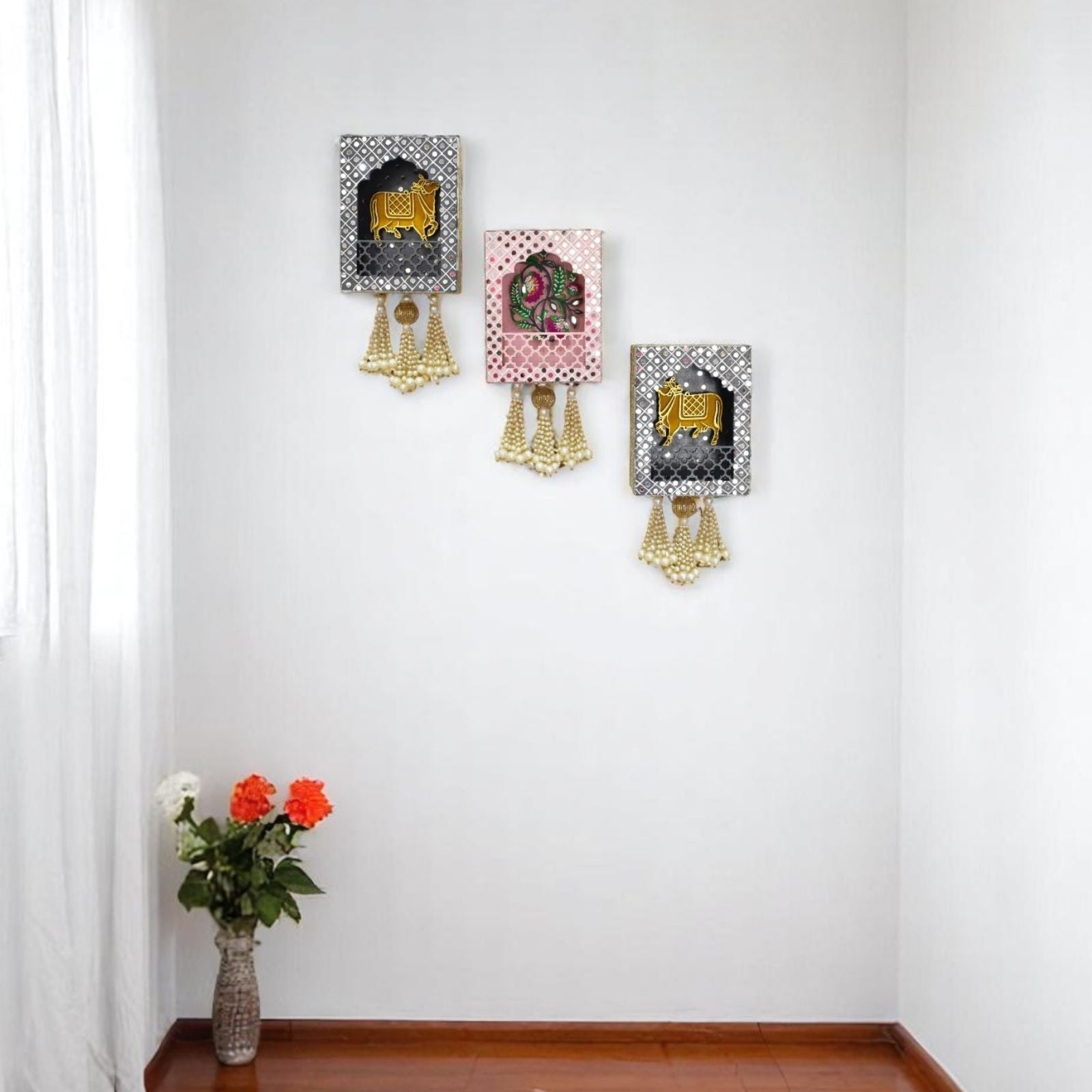 Decorative wall art pieces with gold accents on a white wall, accompanied by a vase of flowers on a wooden floor.