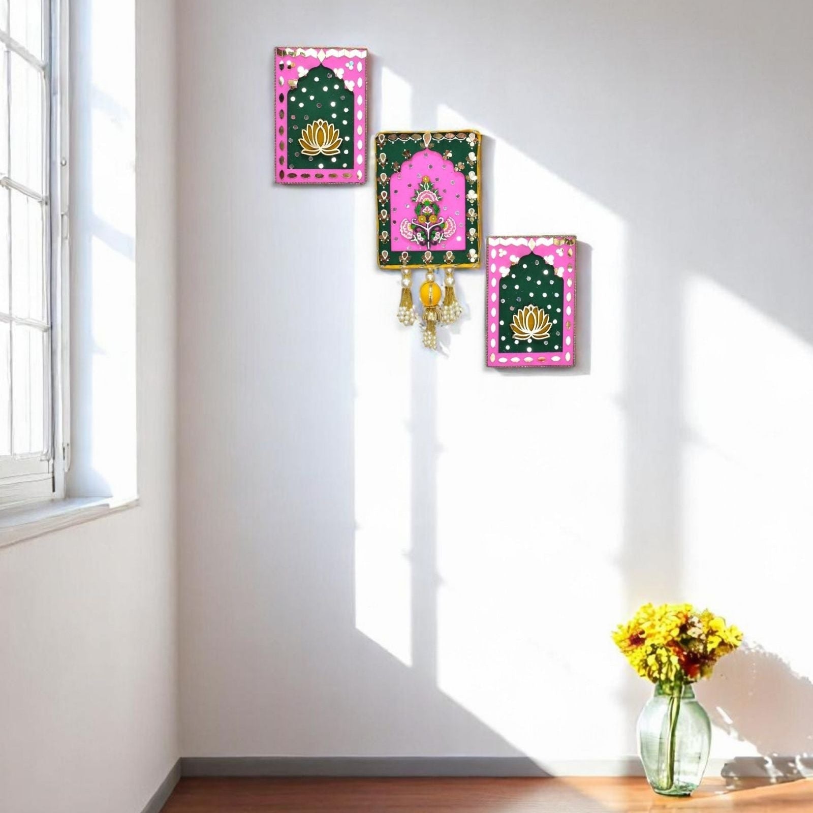 Decorative wall art with pink and green frames on a white wall, sunlit room with a vase of flowers on a table.