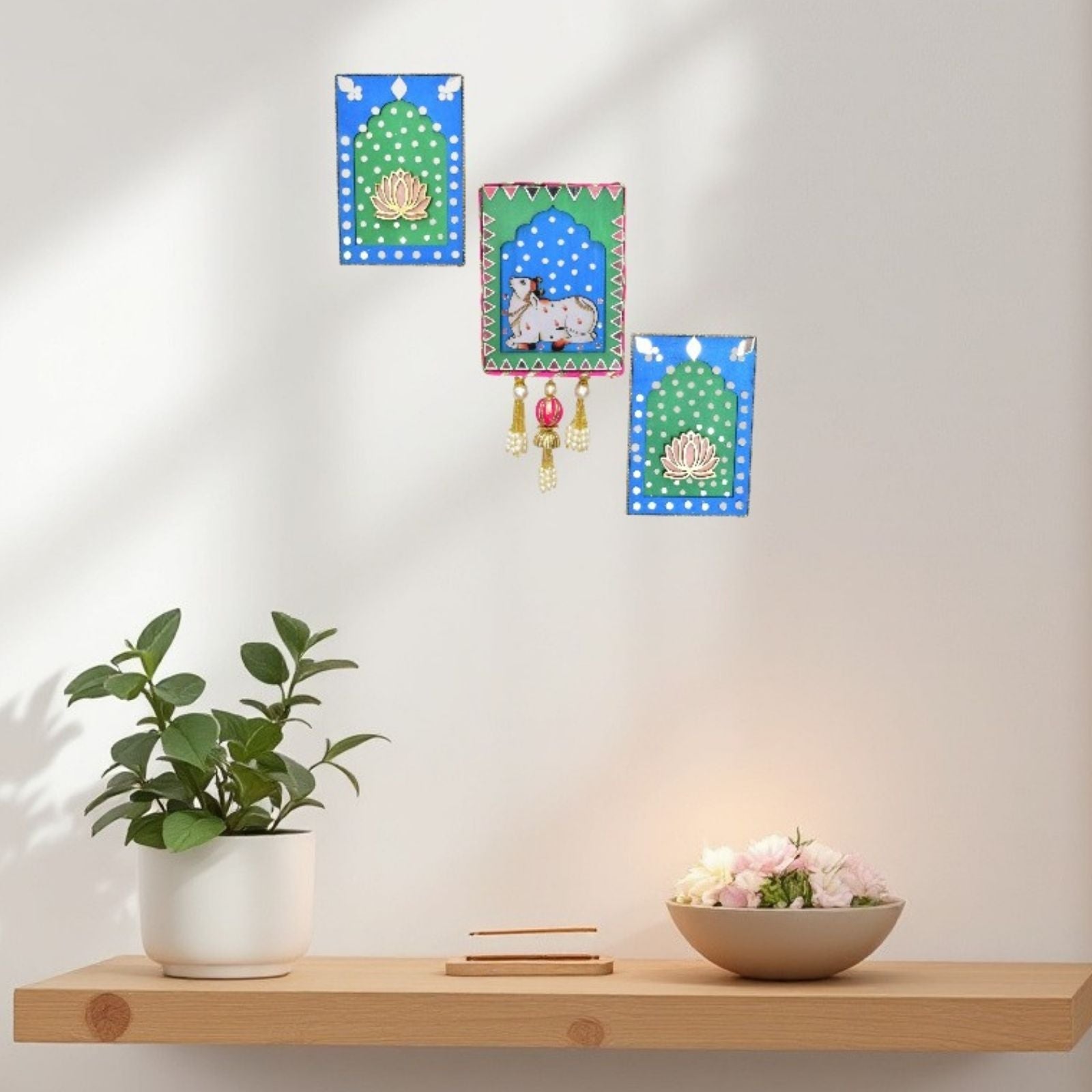 Decorative wall hangings with a plant and bowl on a shelf against a white wall.