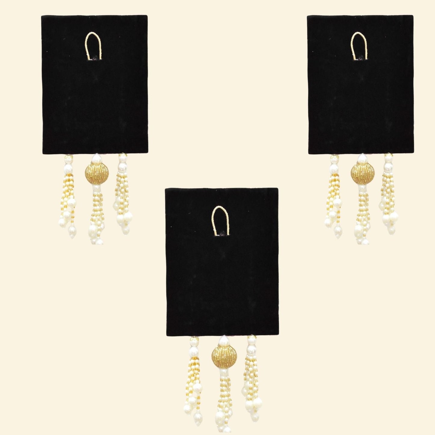 Two pairs of gold and pearl earrings on black display cards against a beige background.