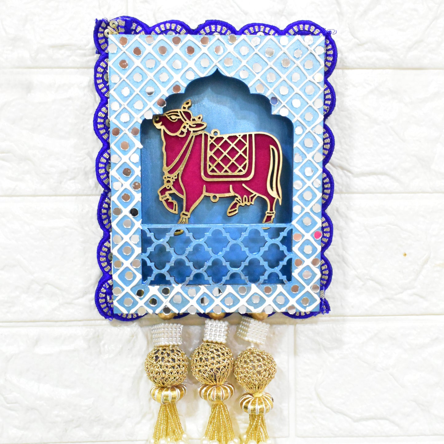 Jharokha Wall Hanging with a blue and white geometric patterned frame, featuring a pink and gold cow figurine, and pearl tassels.