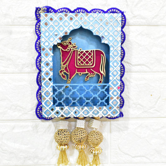 Jharokha Wall Hanging with a blue and white geometric patterned frame, featuring a pink and gold cow figurine, and pearl tassels.