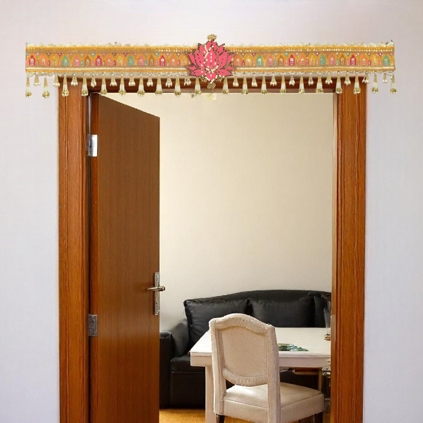 Decorative door toran hanging with a pink flower ornament, leading to a room with a table and chairs.