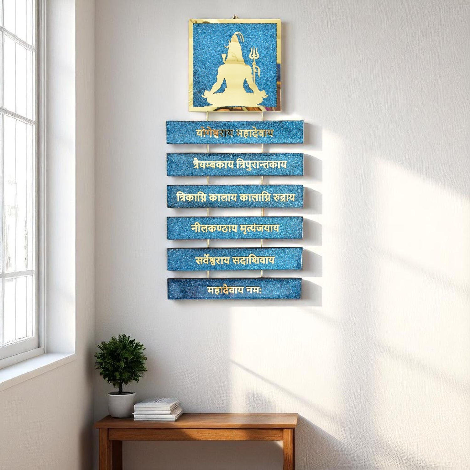 Decorative wall art with blue panels and gold Shiva figure in a room with a window and wooden table.