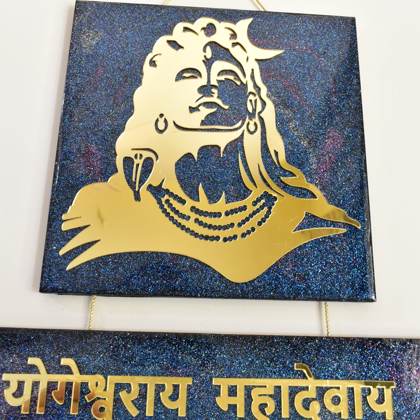 Decorative wall art with gold silhouette of a shiva meditating on a blue glittery background