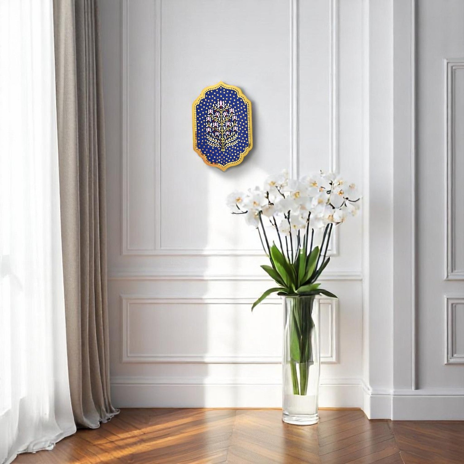 Decorative vase with white flowers on a wooden floor against a white wall with a decorative blue and gold wall piece.