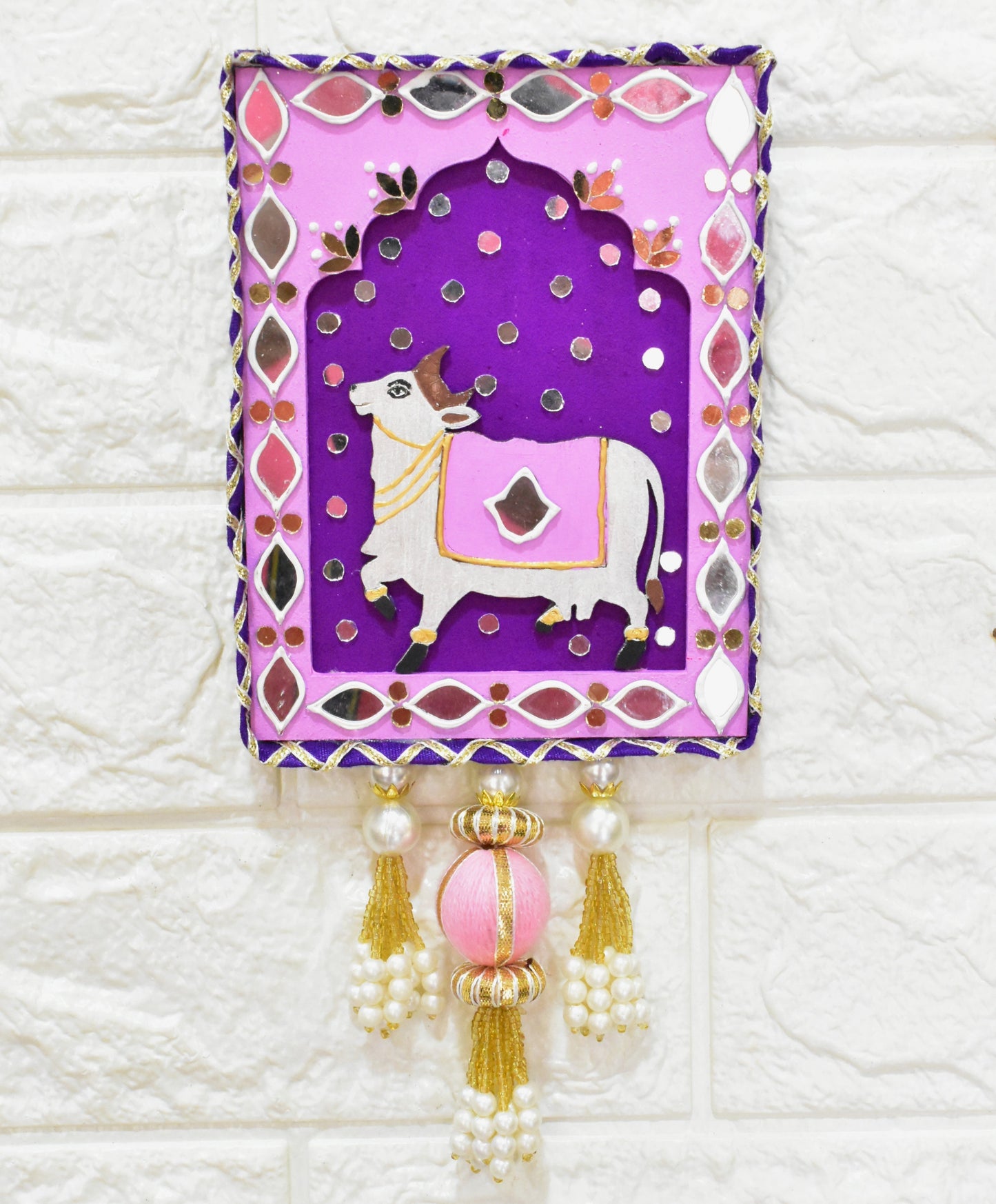 Decorative wall hanging with a purple background and cow illustration on a textured white wall.
