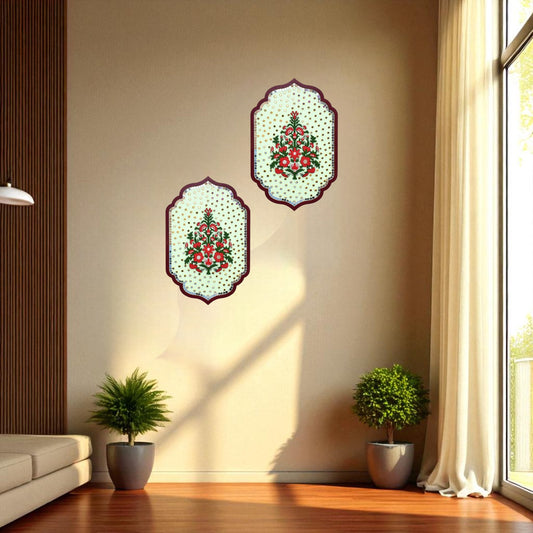 Two decorative wall art pieces with floral designs on a beige wall, with plants and a sofa in the foreground.