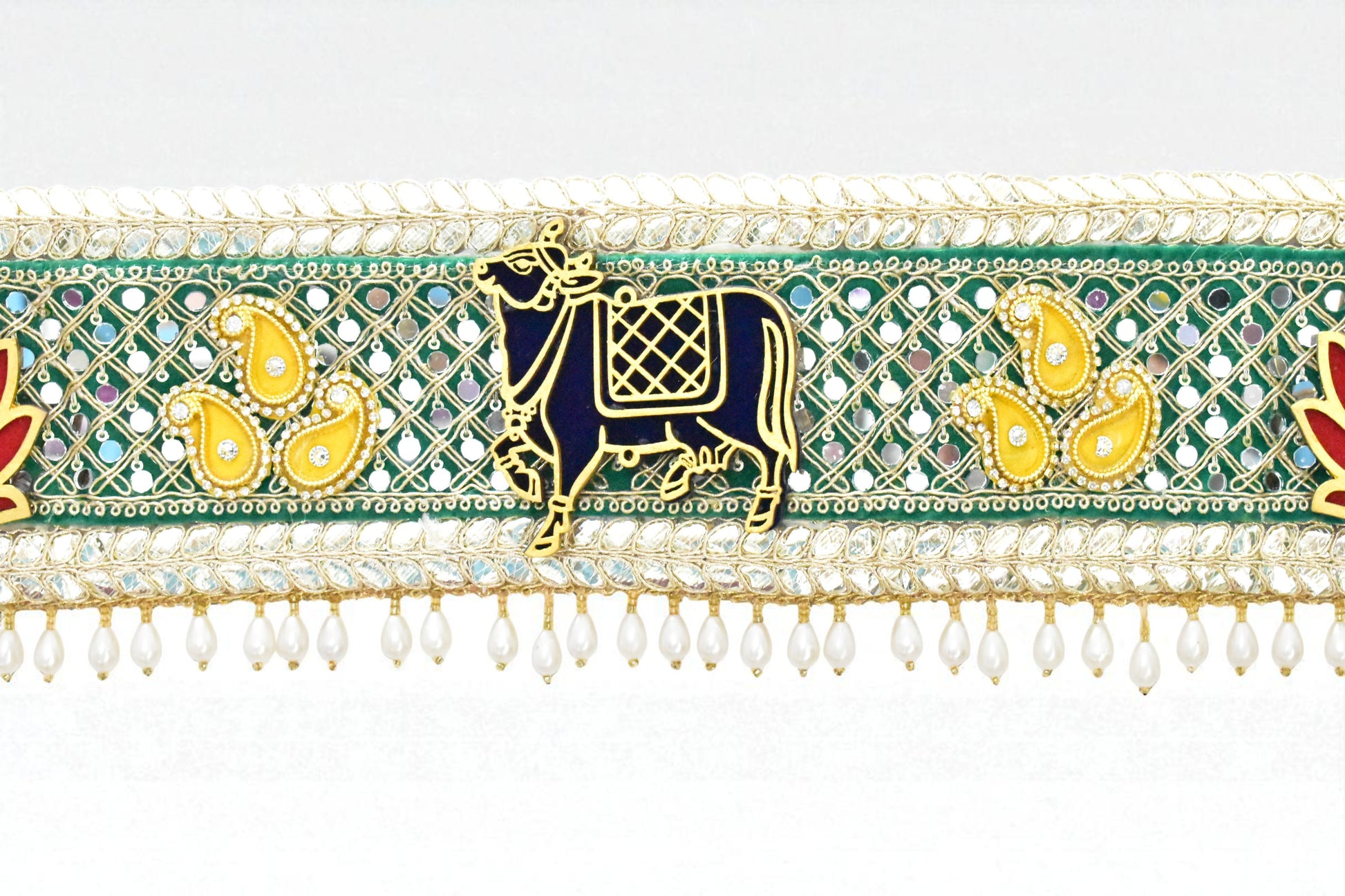 Decorative toran with a cow design, green and gold colors, and white beads.