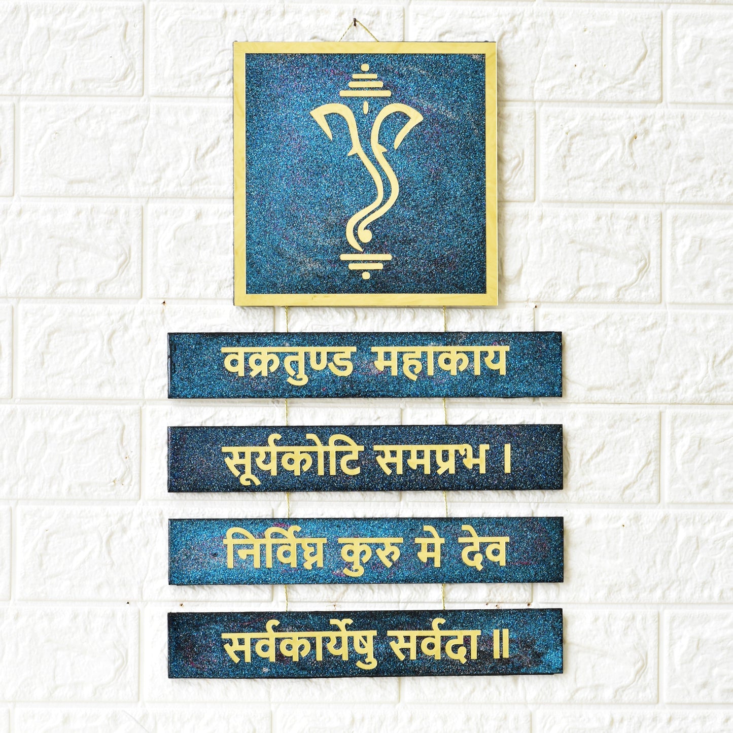 Decorative wall art with Ganesha symbol and Sanskrit text on a textured white wall.