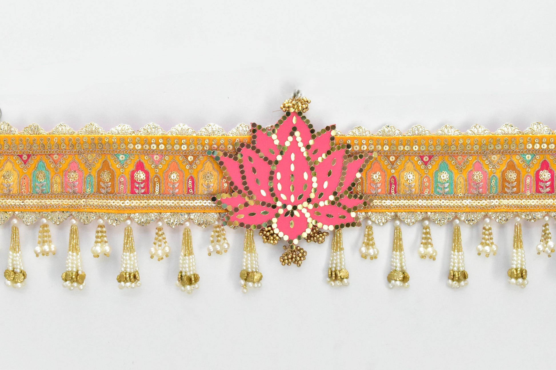 Decorative toran with pink floral design and gold tassels on a white background