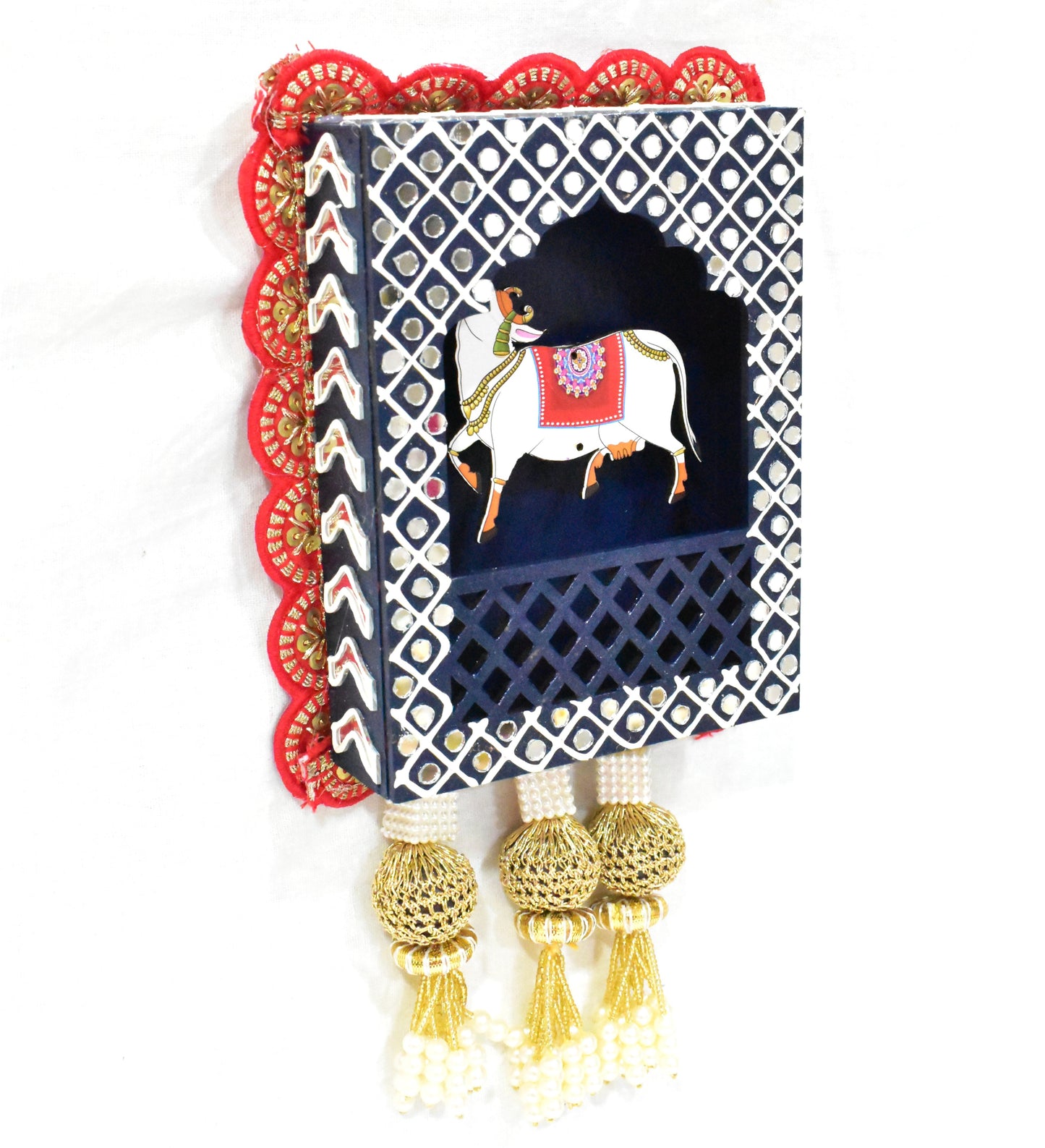 A decorative wall hanging featuring a traditional Indian design with a cow and lotus motifs, adorned with a tassel.