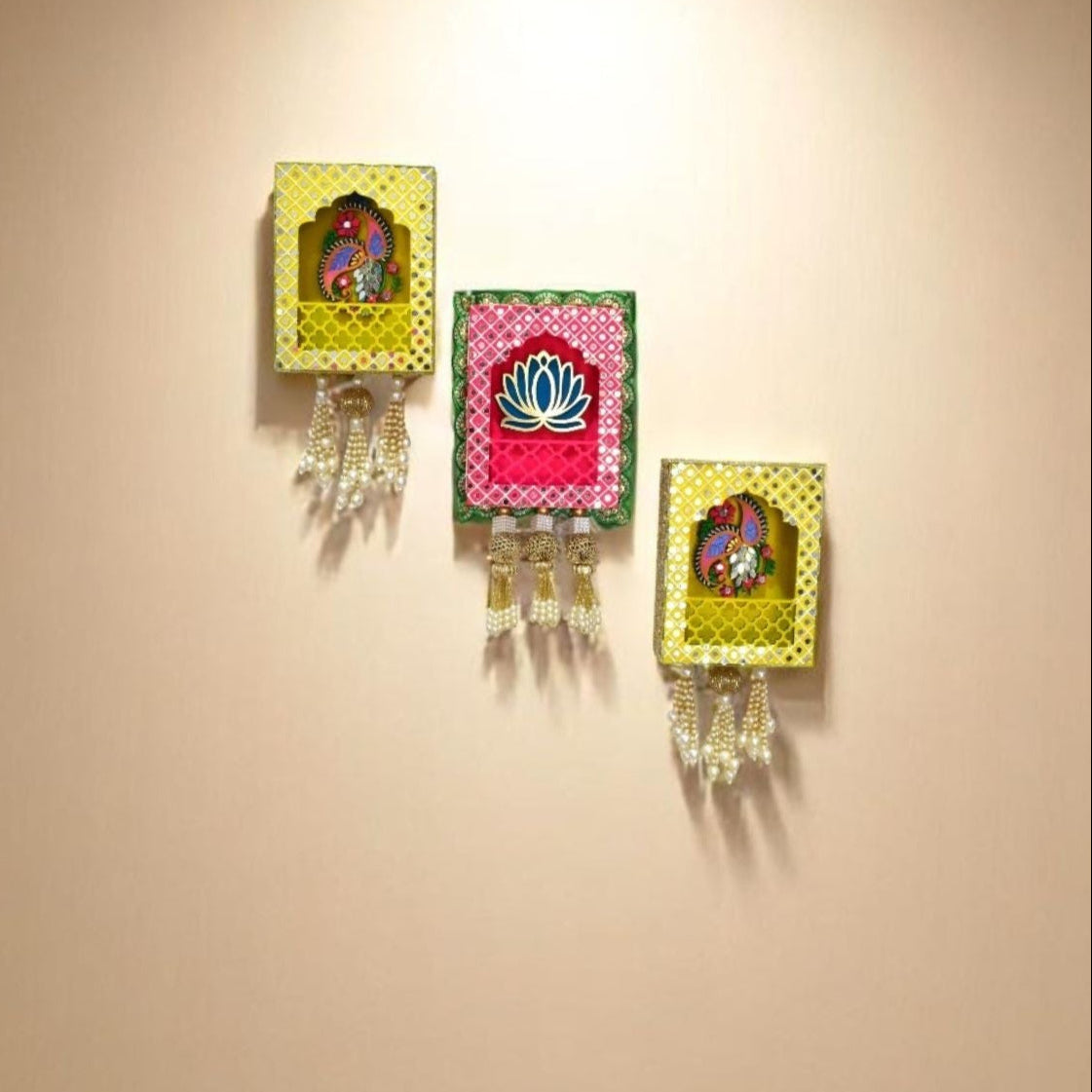 Three wall hangings of pink and yellow with decorative mirrors, beads and pearls tassels on a beige living room wall