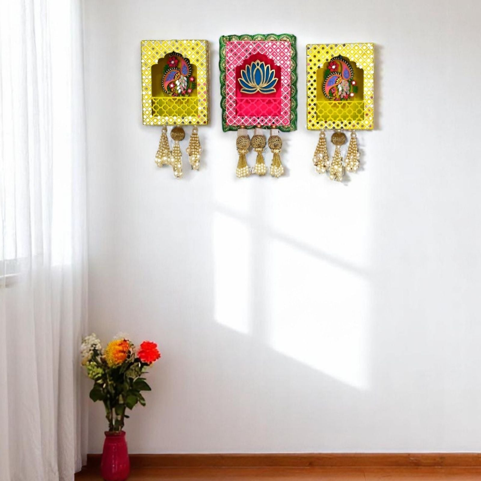 Three wall hangings of pink and yellow with decorative mirrors, beads and pearls tassels in the living room.