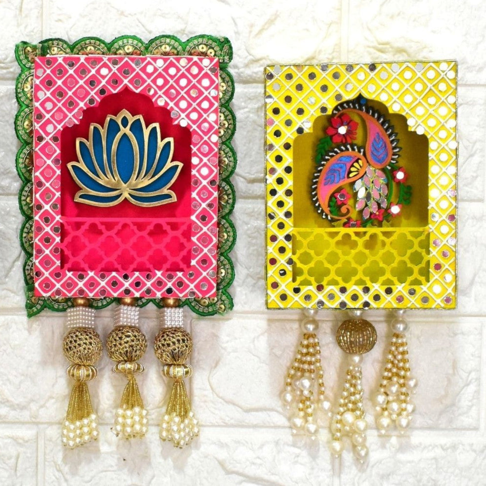Close up of wall hangings of pink and yellow with decorative mirrors, beads and pearls tassels on a white background