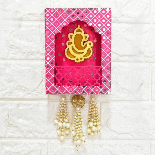 Pink decorative wall hanging Jharokha with gold Ganesh symbol, mirrors and pearl beads on a white textured background.