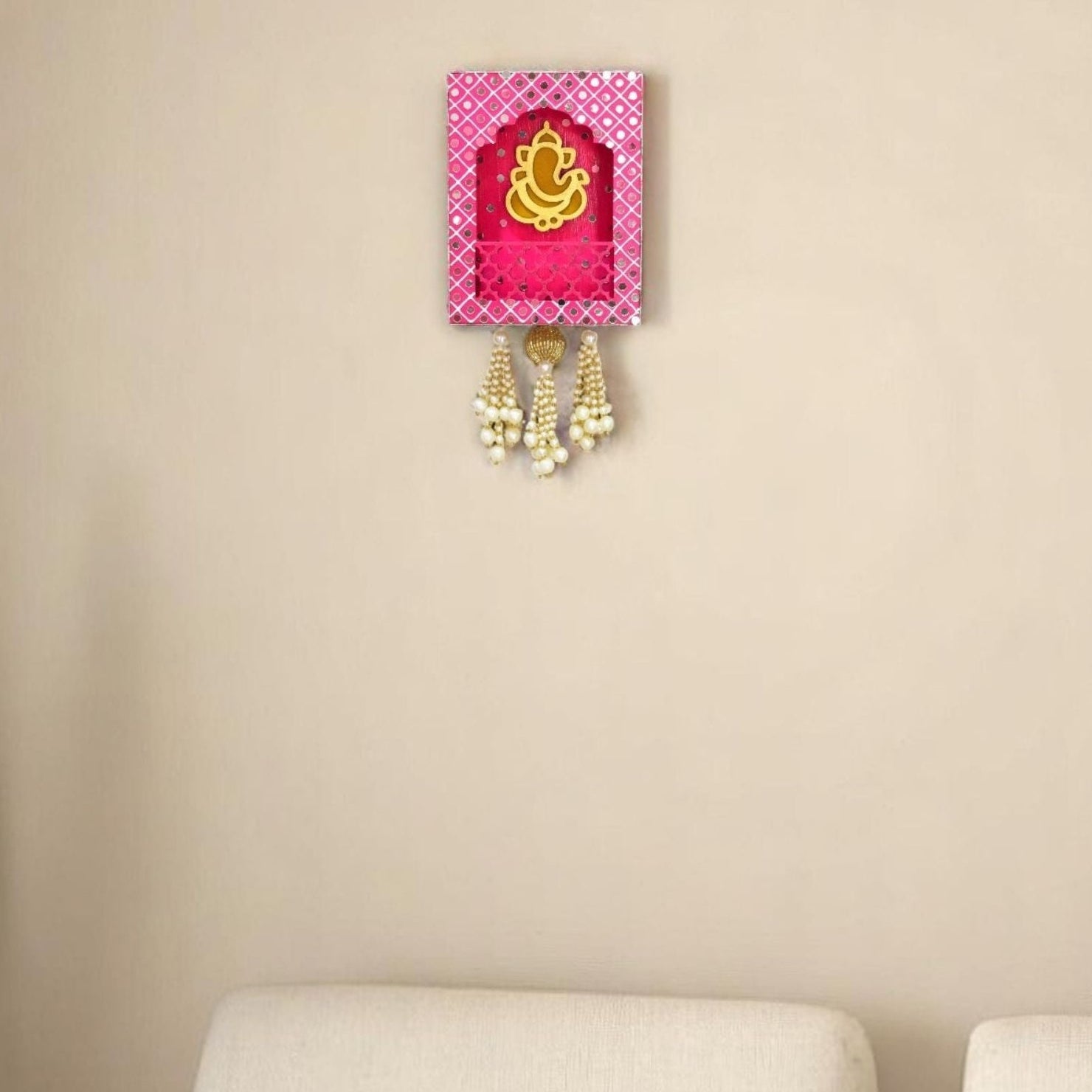 Pink decorative wall hanging Jharokha with gold Ganesh symbol, mirrors and pearl beads in the living room.