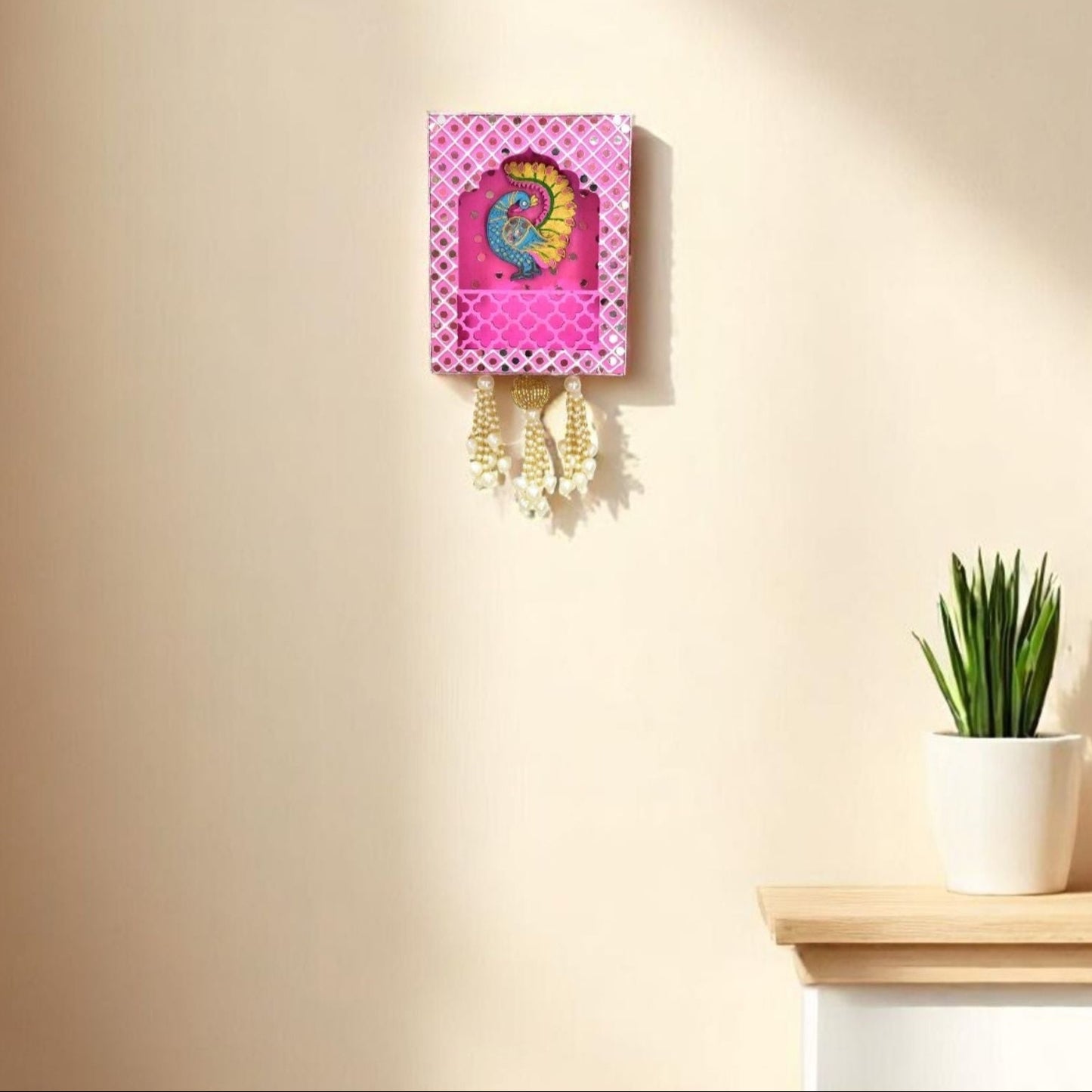 Decorative Pink Wall Jharokha with peacock design and mirrors on a beige background next to a plant in the living room.