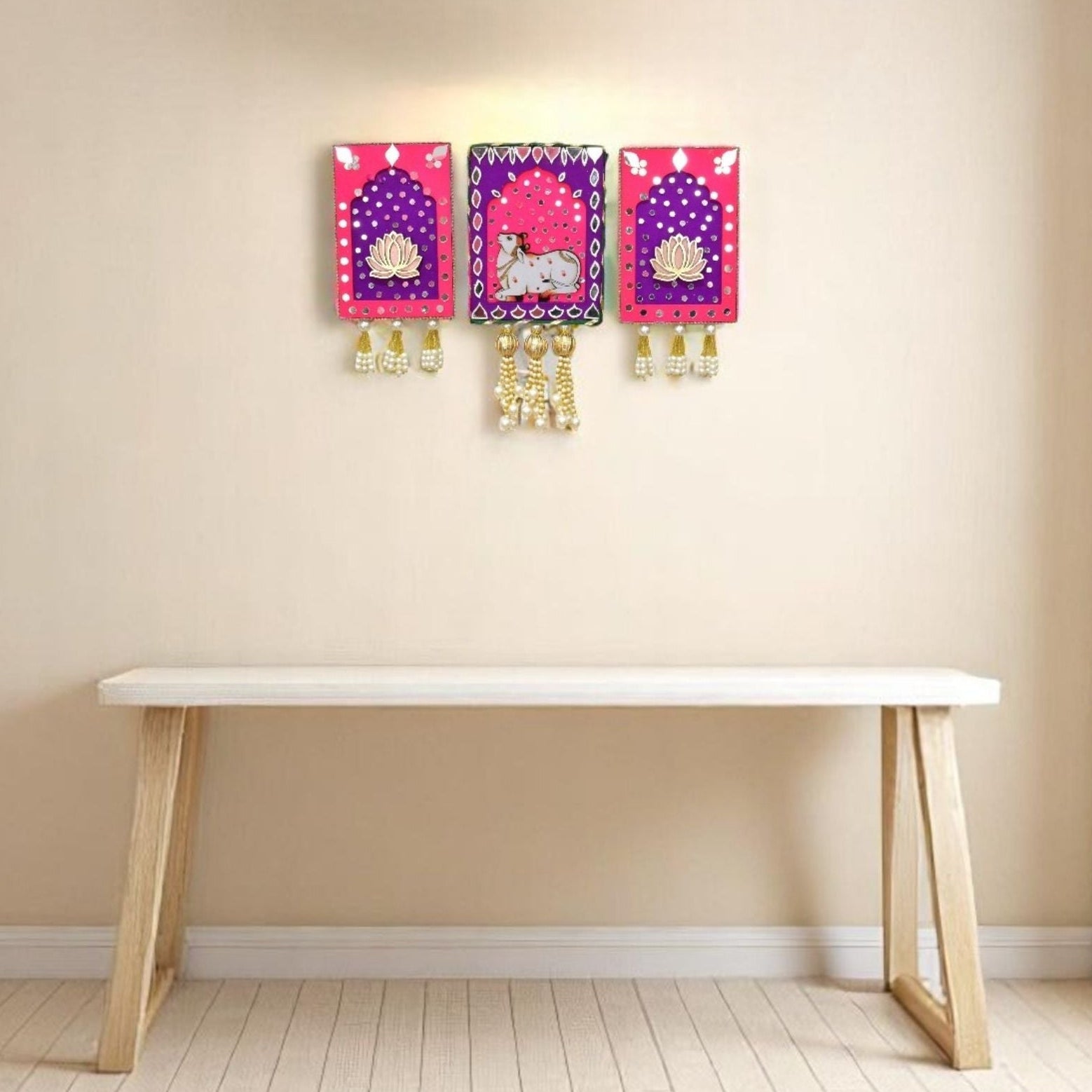 Pink and purple jharokha wall art with cow and lotus with mirrors and gold beads and pearl tassels in the living room.