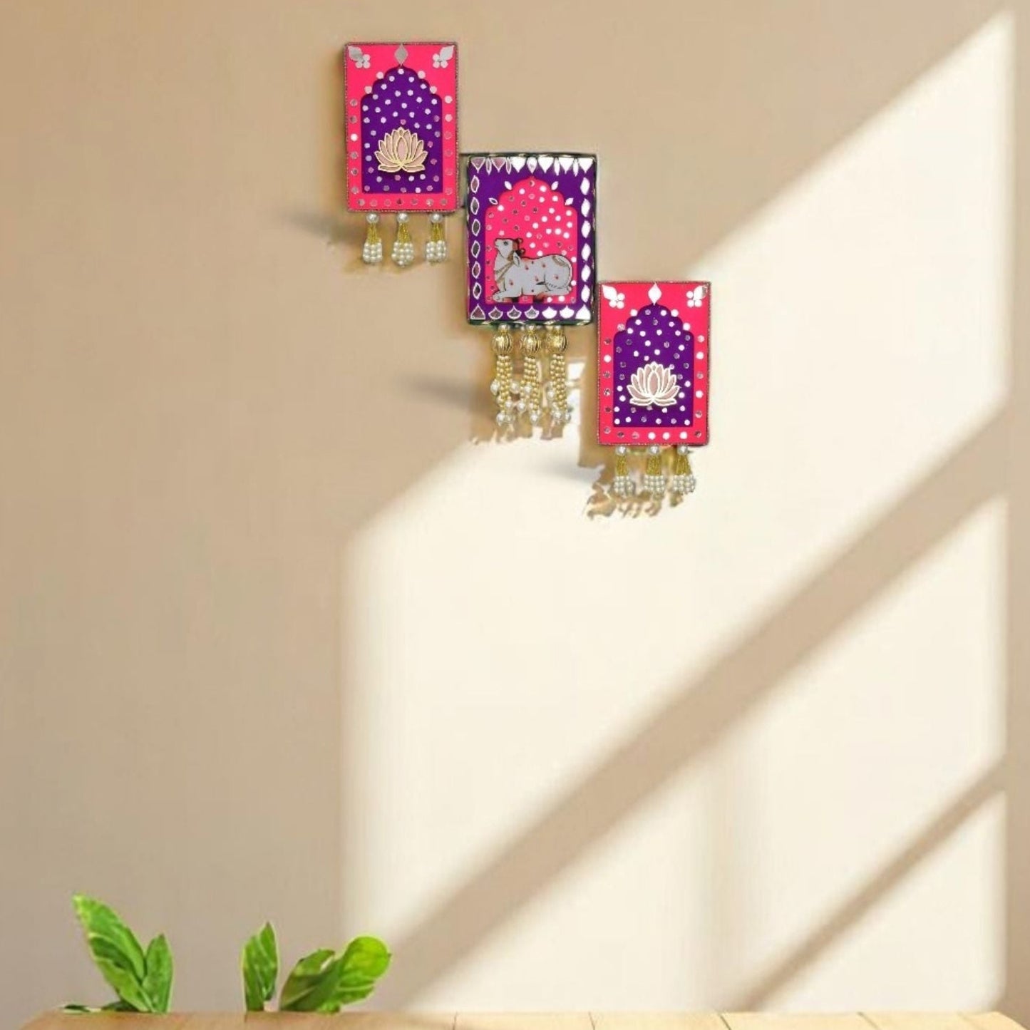 Pink and purple jharokha wall art with cow and lotus with mirrors and gold beads and pearl tassels in the living room.