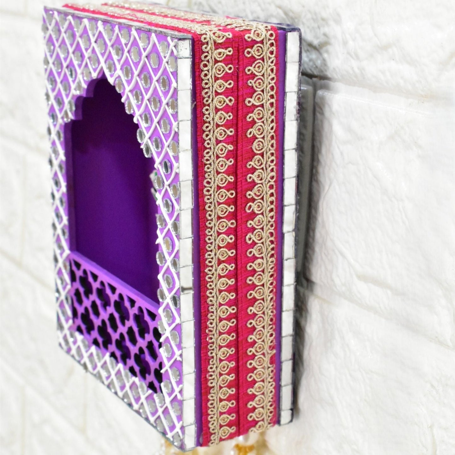 Jharokha wall hanging with purple interior and pink and gold tassels on a white background