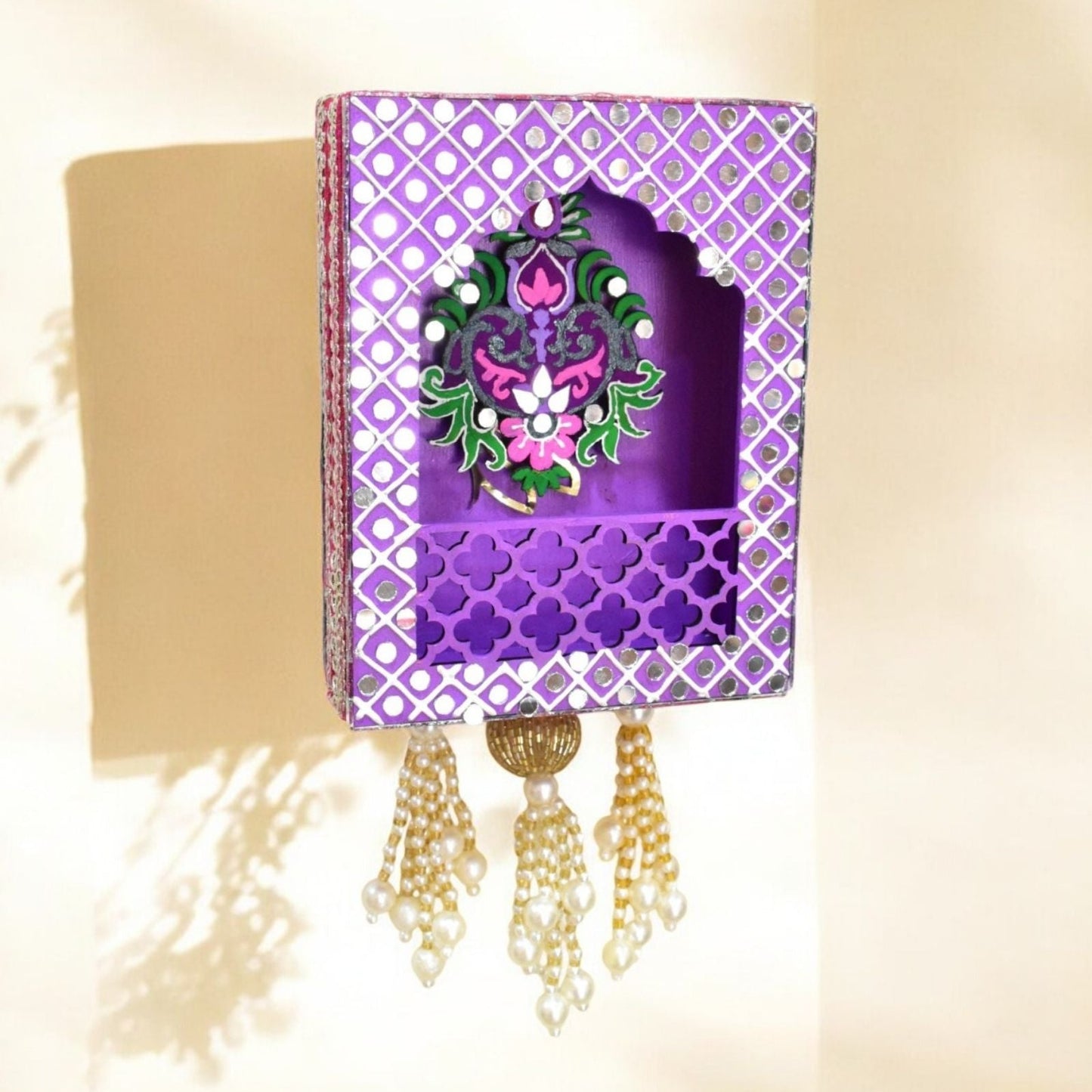 Decorative purple jharokha wall hanging with intricate design and tassels on a beige background