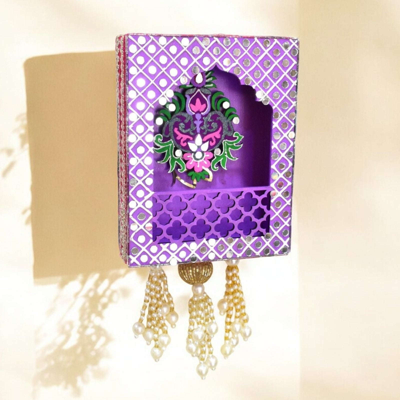 Decorative purple jharokha wall hanging with intricate design and tassels on a beige background