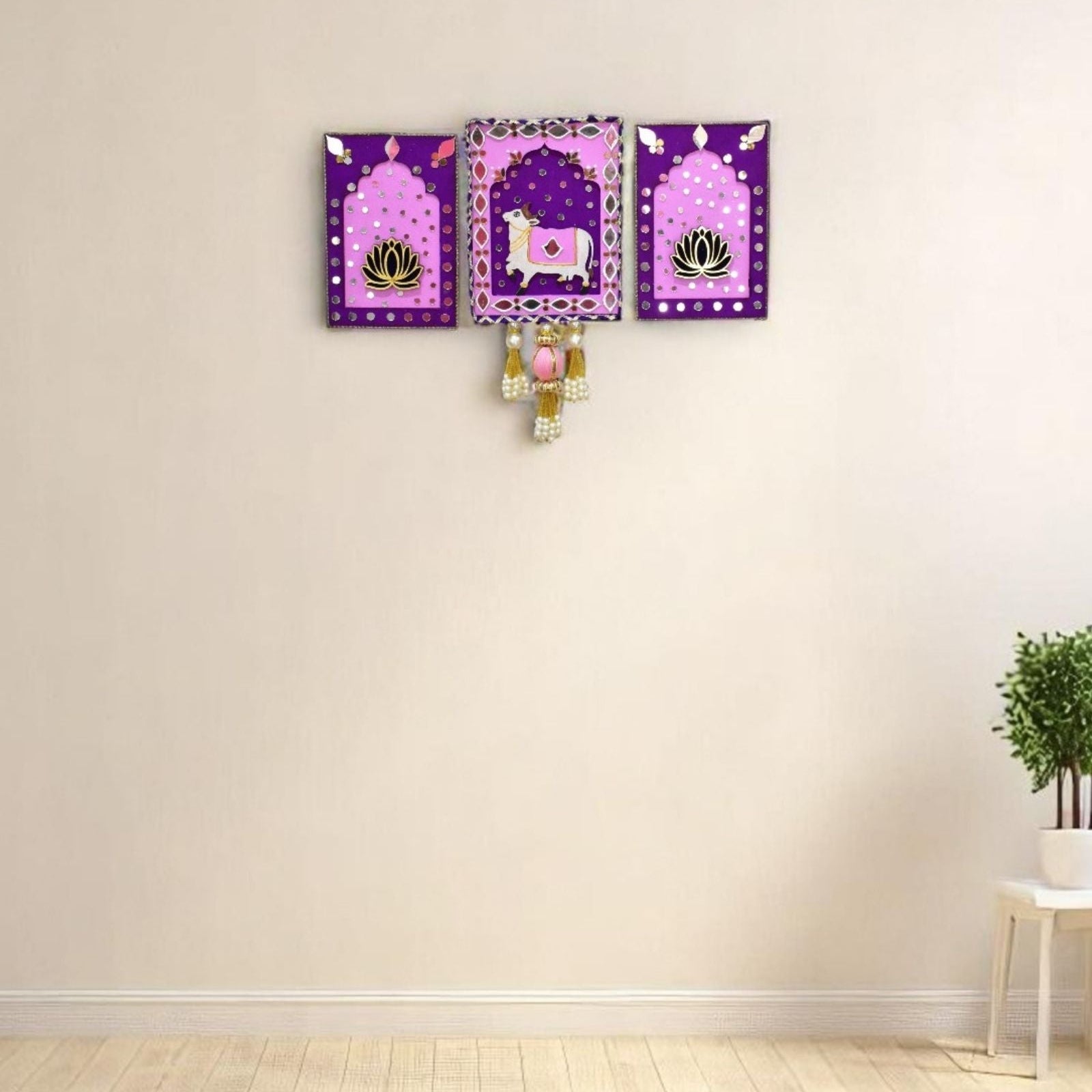 Set of three decorative jharokha with pink & purple borders and centers featuring a cow and lotus design on a living room wall.