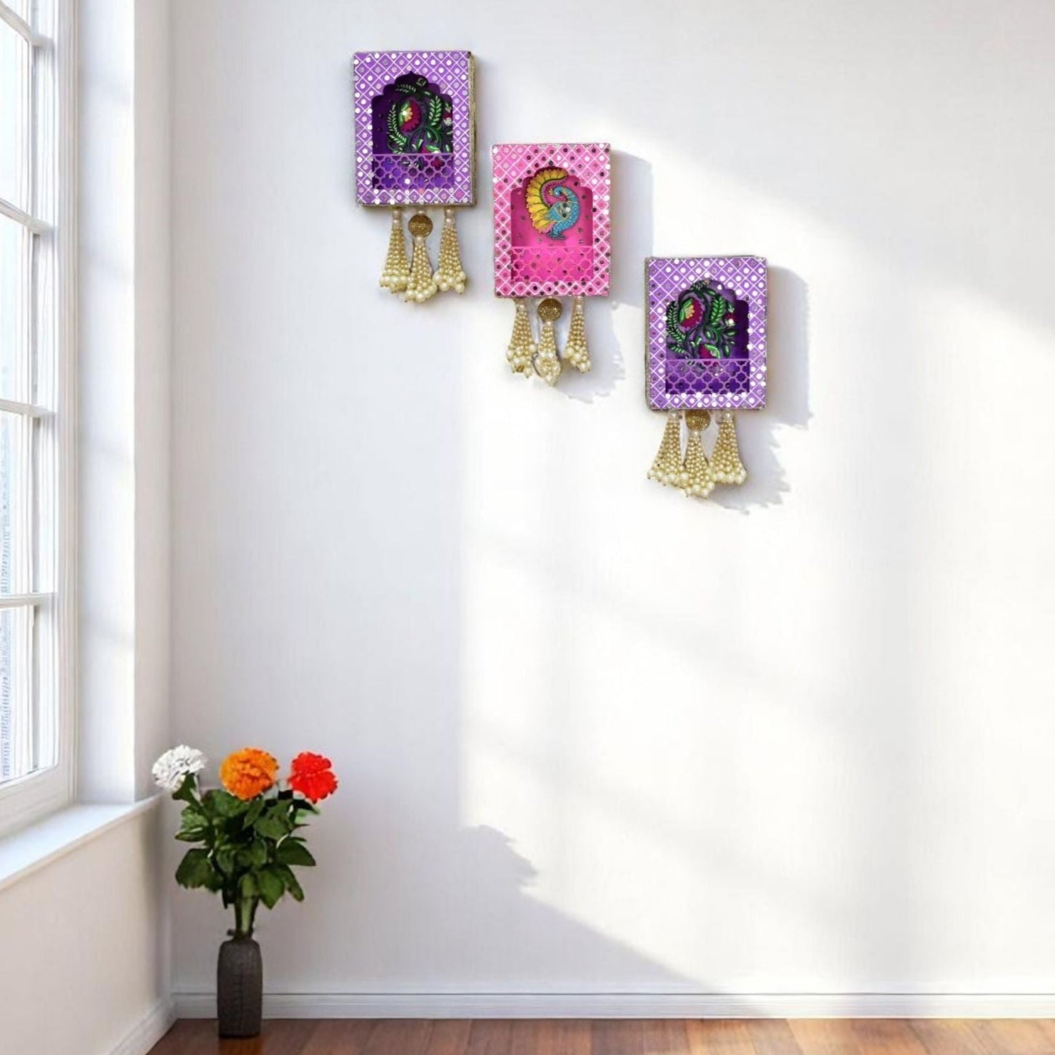 Decorative wall art in pink and purple with peacock and floral design on a white wall, next to a window with flowers on a wooden floor.