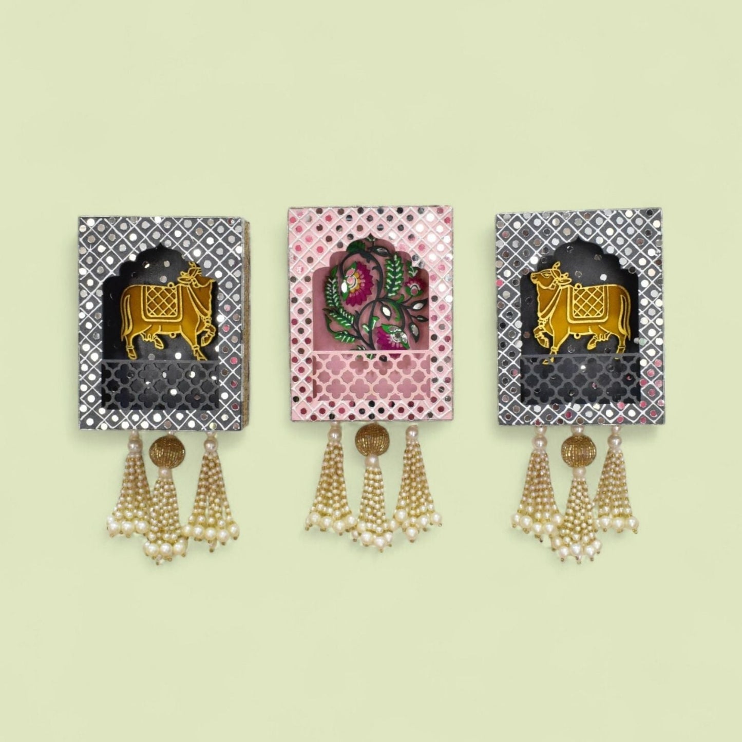 Three decorative wall hangings with cow and floral design and tassels on a light beige background