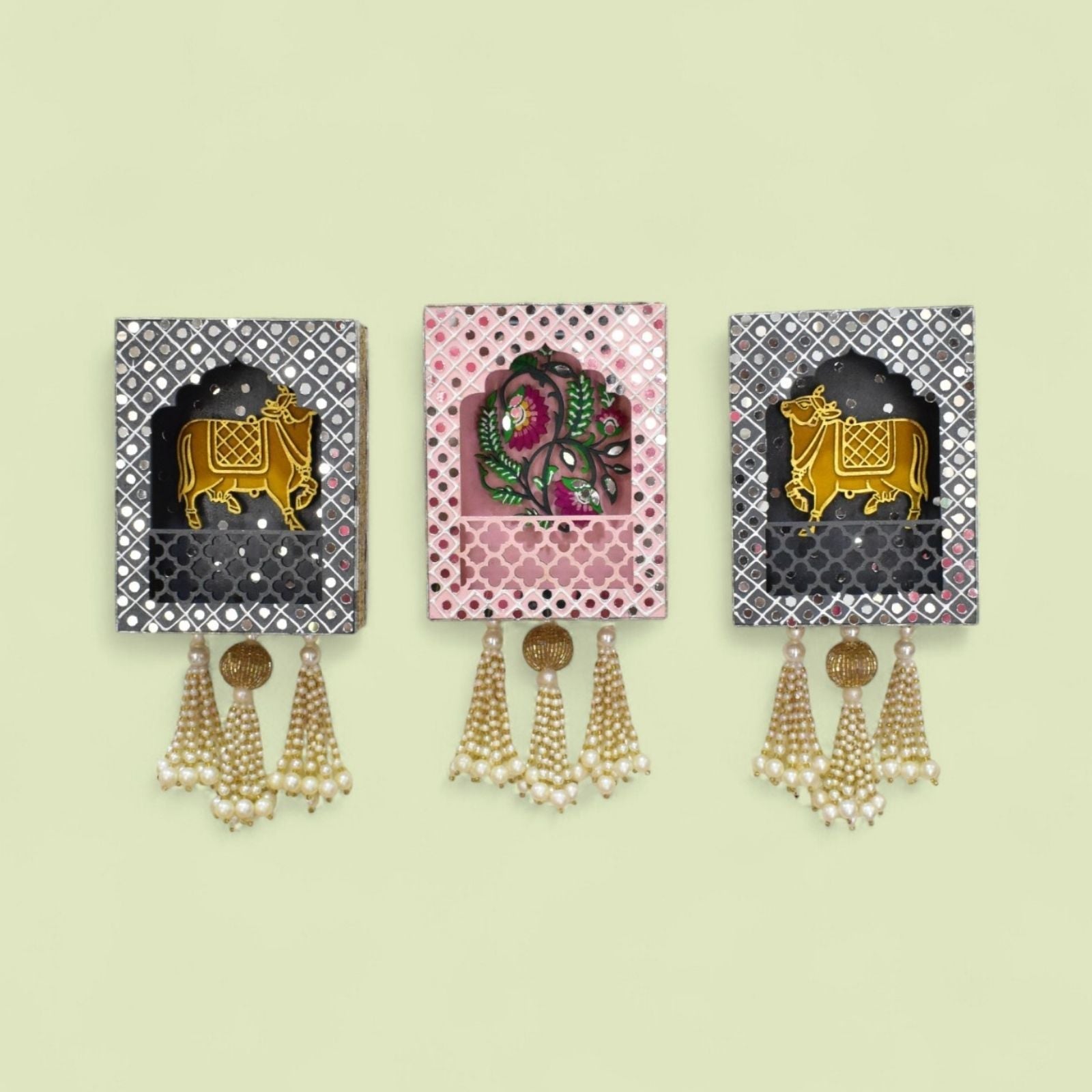 Three decorative wall hangings with cow and floral design and tassels on a light beige background