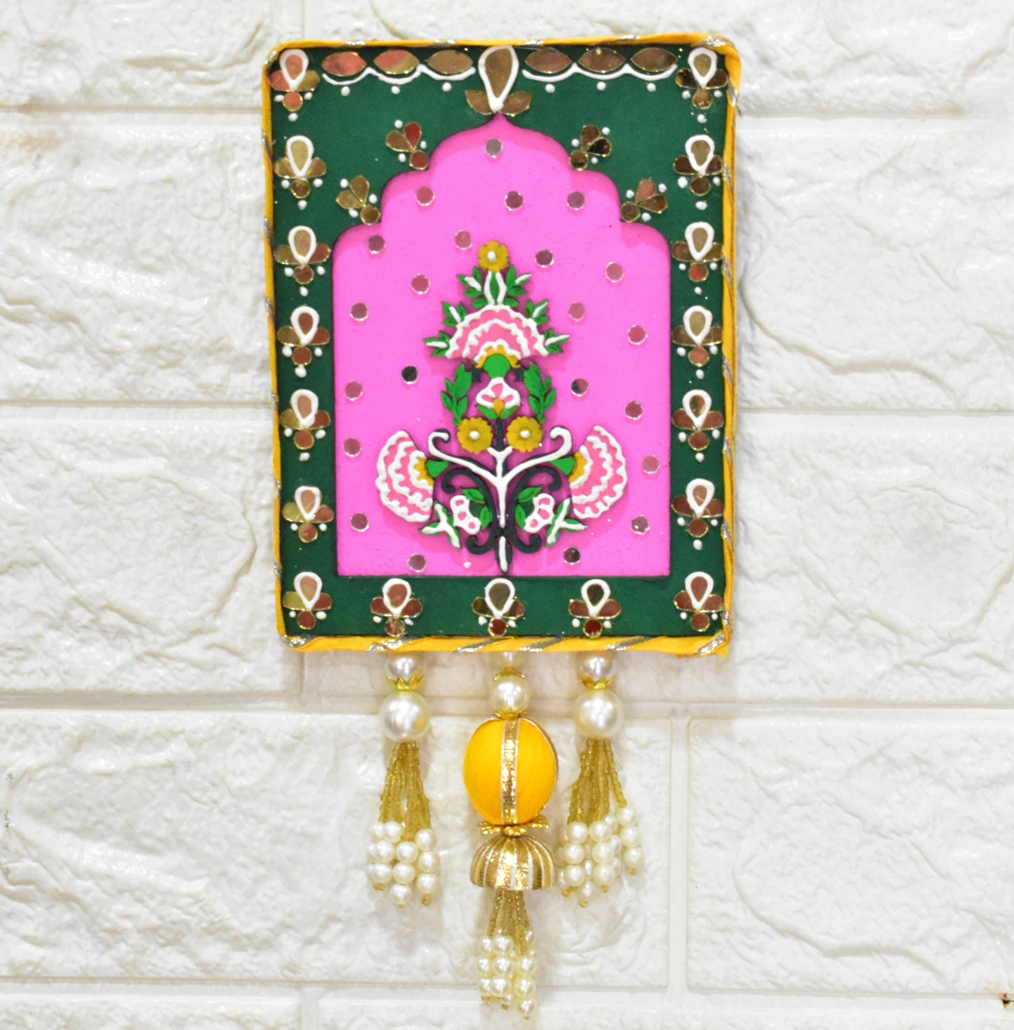 Pink and green wall art with floral design with beads and pearl tassels on a white textured wall