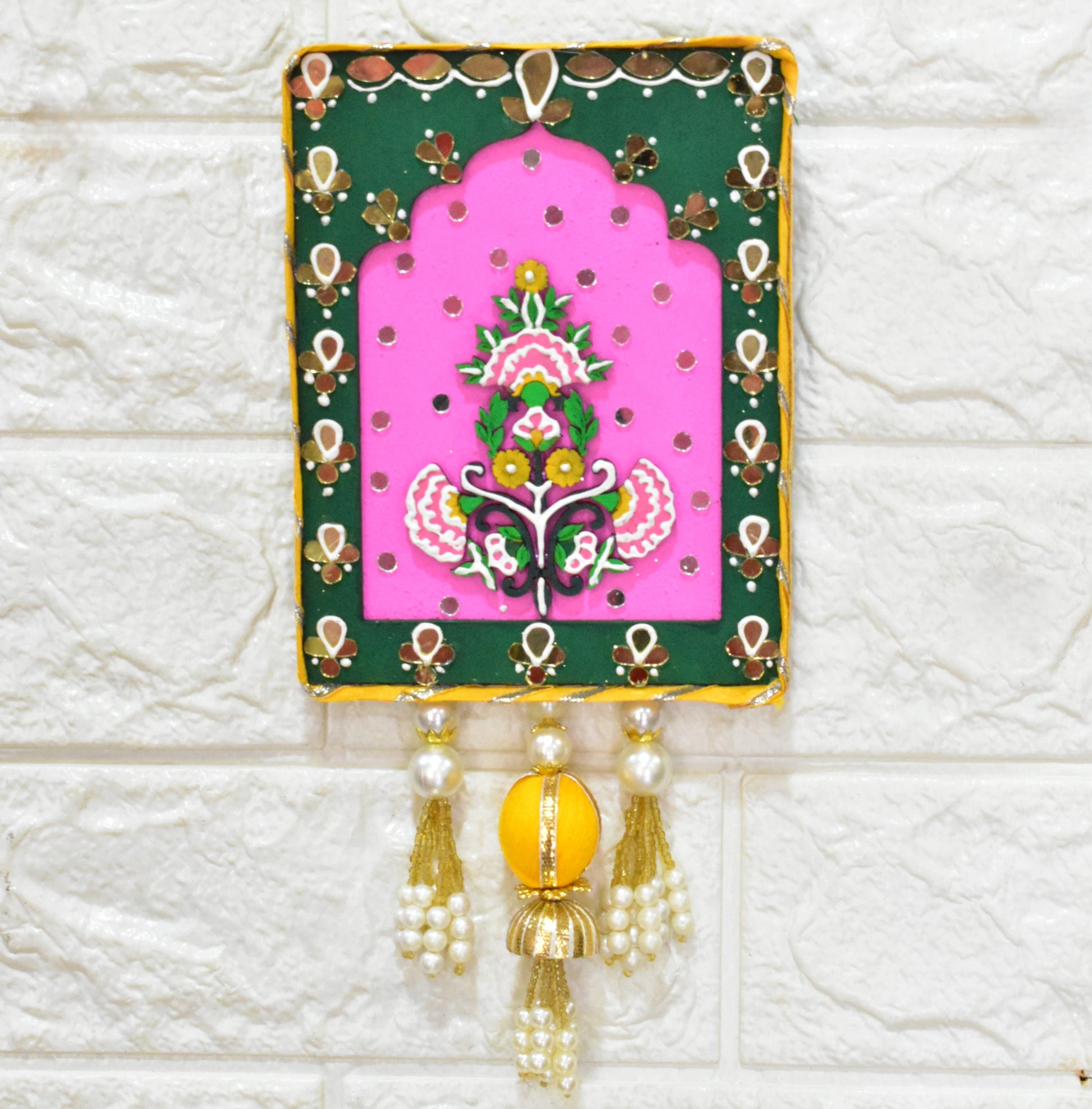 Pink and green wall art with floral design with beads and pearl tassels on a white textured wall