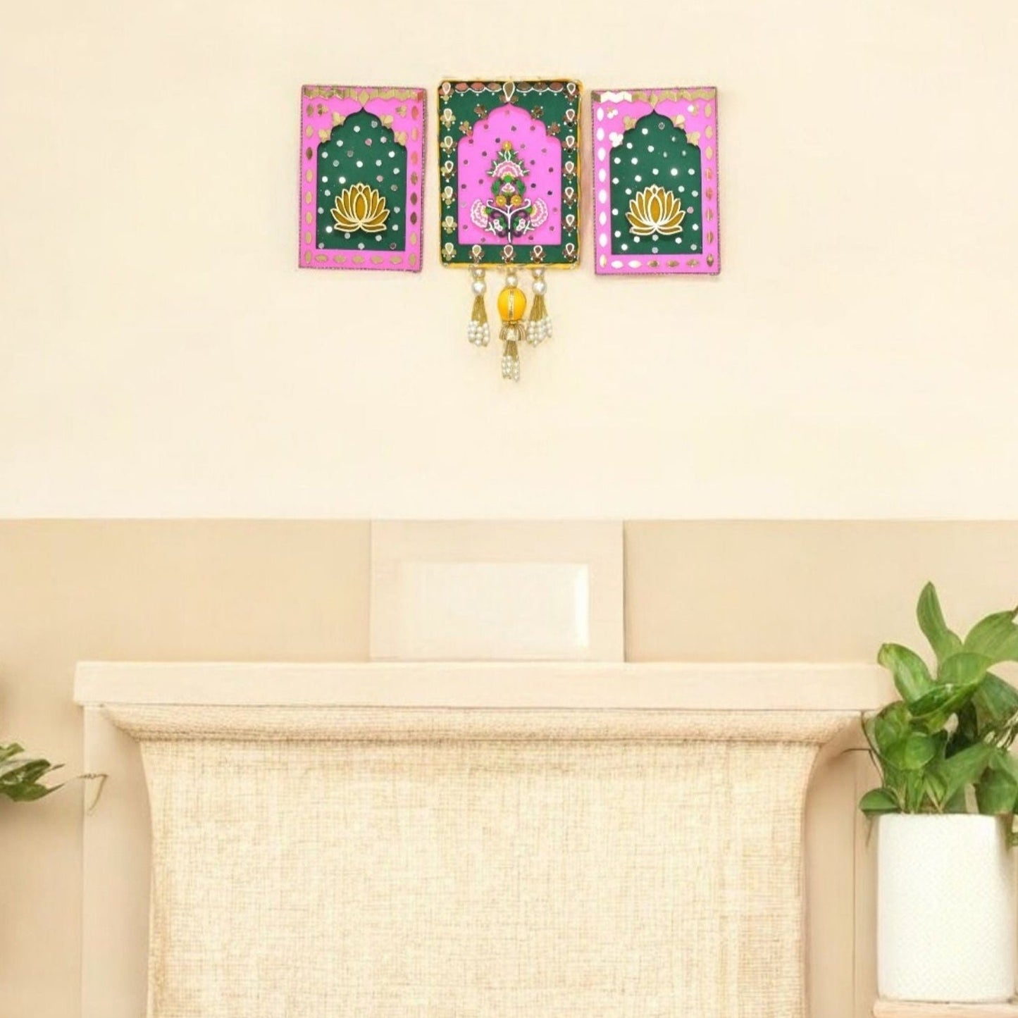 Pink and green wall art with floral design on a cream living room wall with beads and pearl tassels.