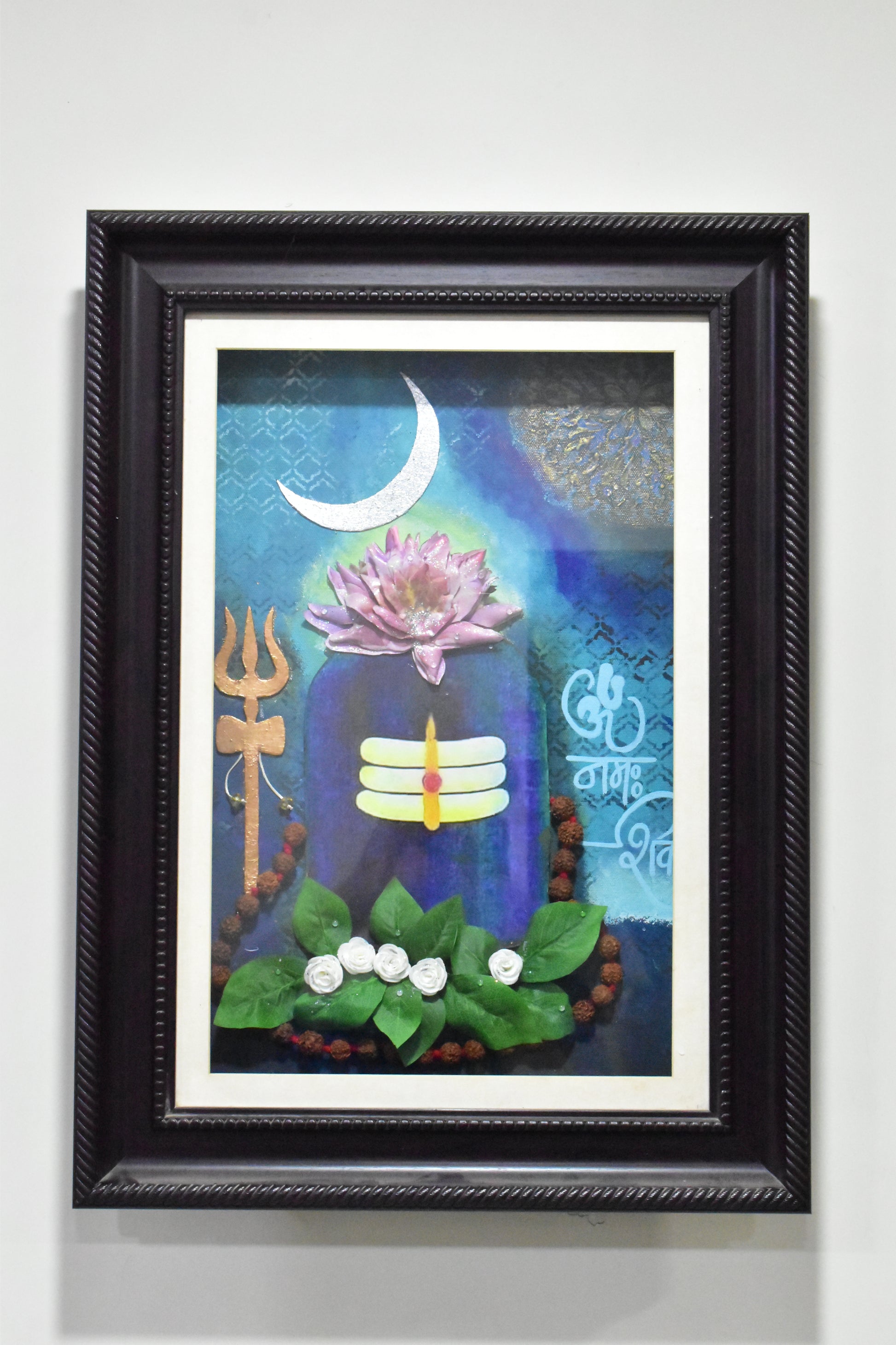 Framed Shivling artwork with a colorful design featuring a flower, moon, and other elements on a white wall.